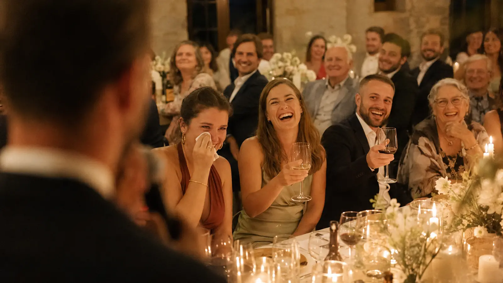 Une tablée d'invités qui éclate de rire pendant un discours.